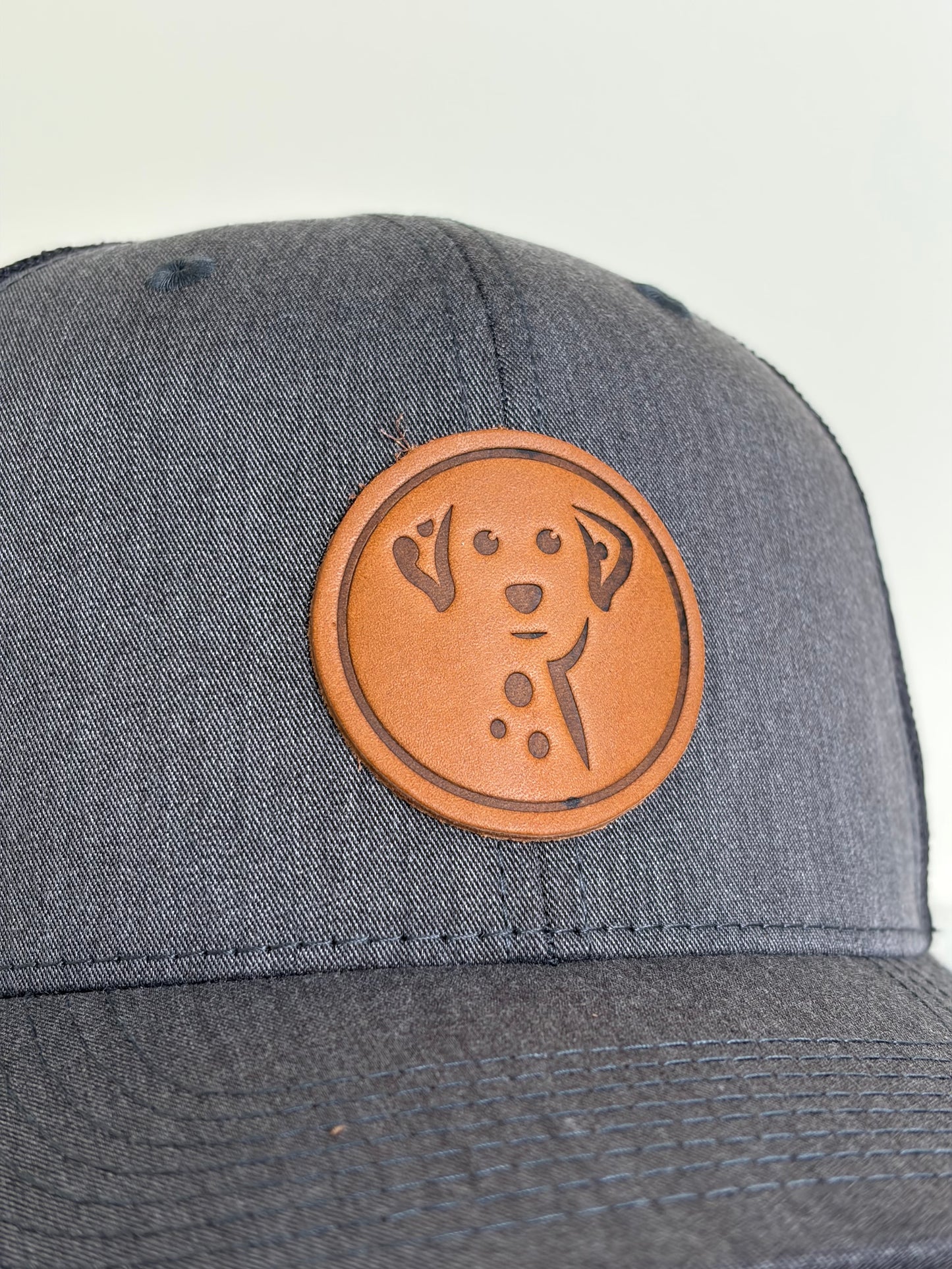 Gray cap with a brown leather patch featuring a dog design on a light gray background