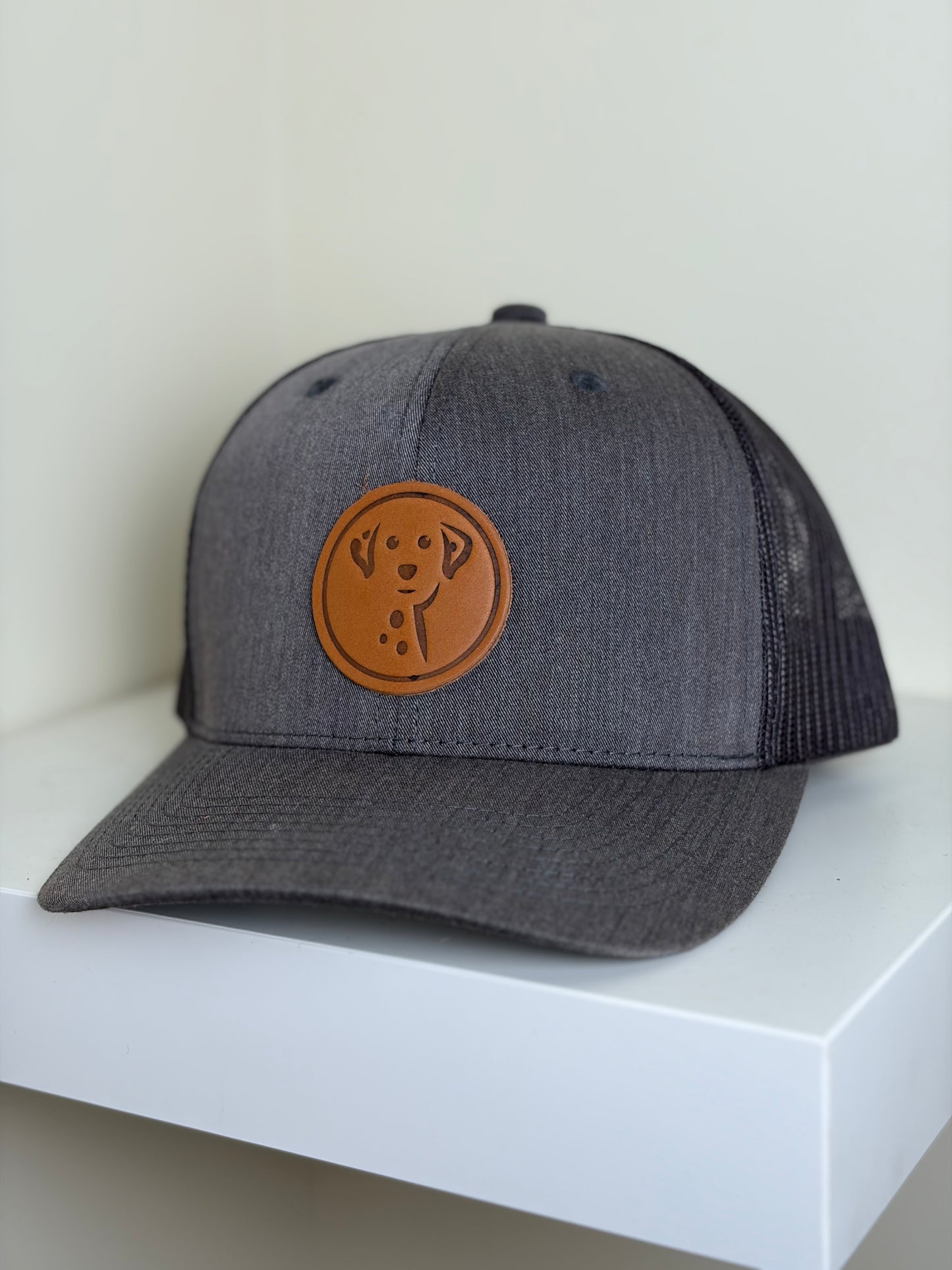 Gray cap with brown leather patch featuring a dog logo on a white surface.
