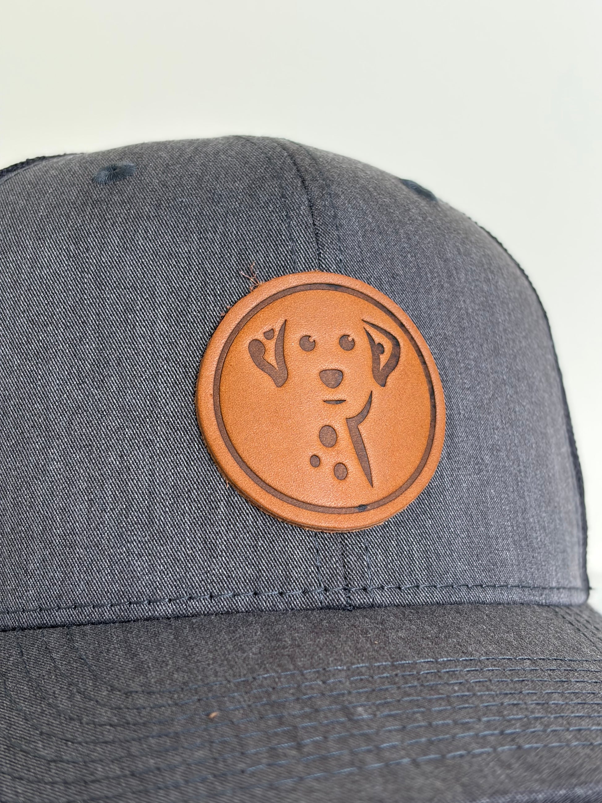 Gray cap with a brown leather patch featuring a dog design on a light gray background